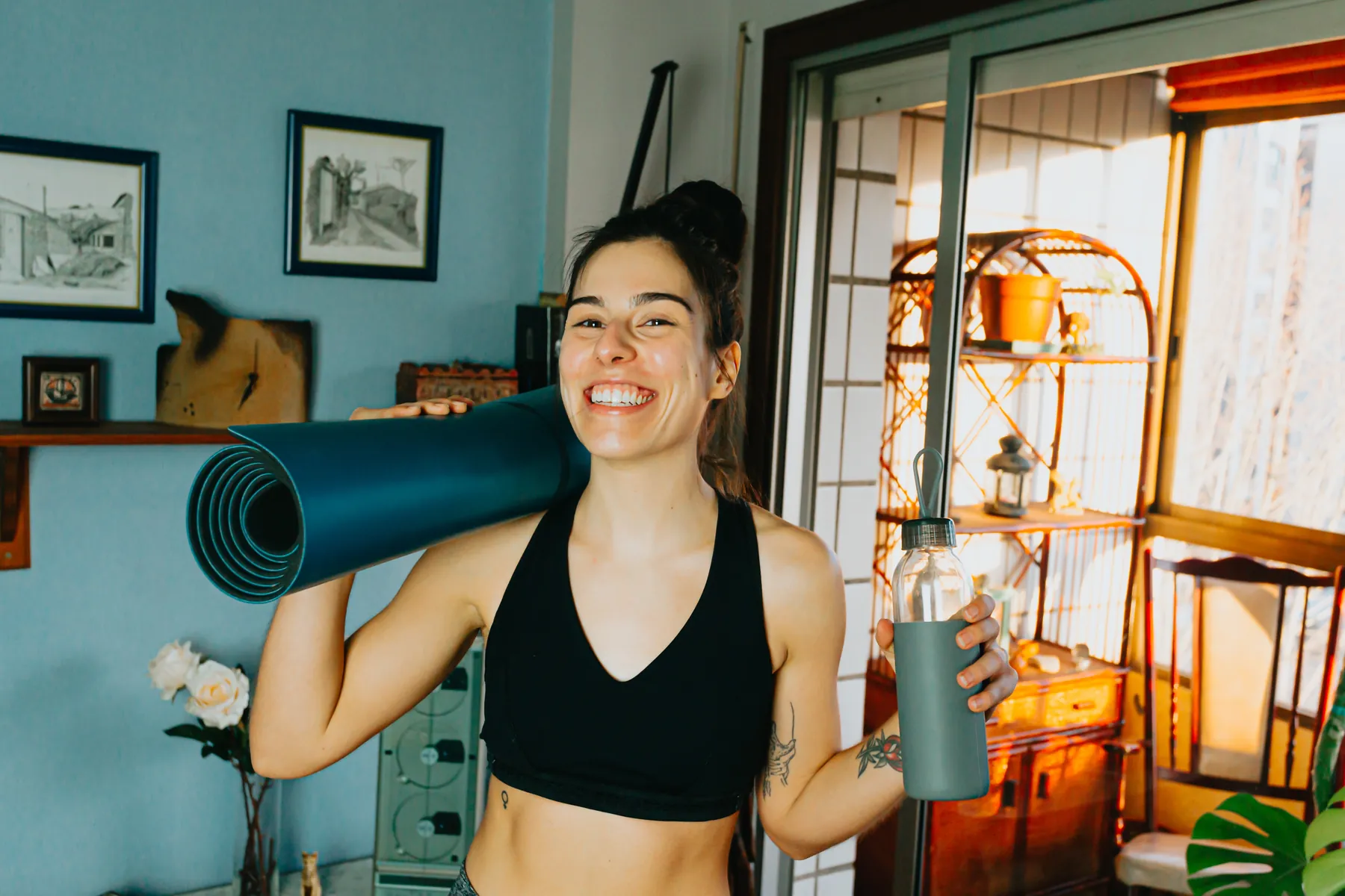 A smiling woman at home with a yoga mat over her shoulder